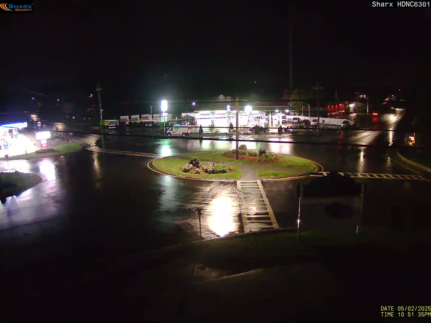 A gas station and roundabout are seen at night in the rain.