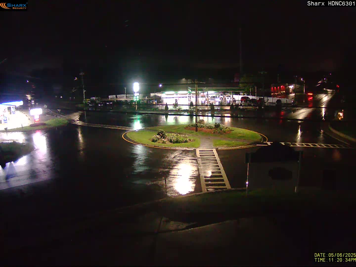 A rain-slicked roundabout at night, illuminated by the lights of nearby gas stations and businesses.