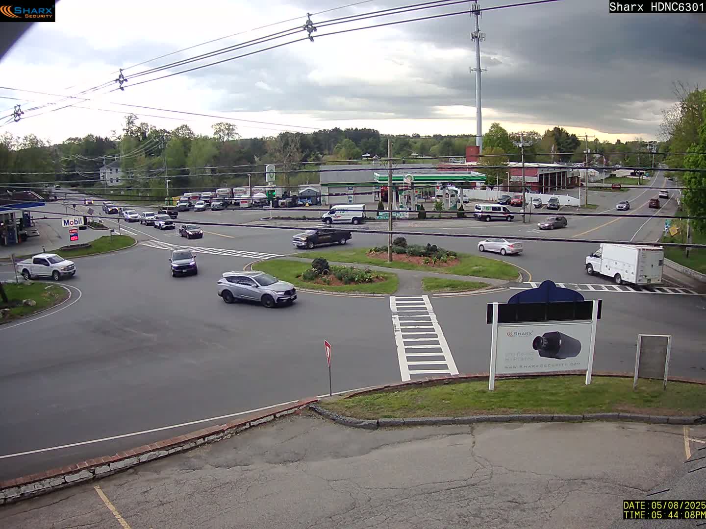 Several cars are navigating a roundabout and intersecting roads under a partly cloudy sky.