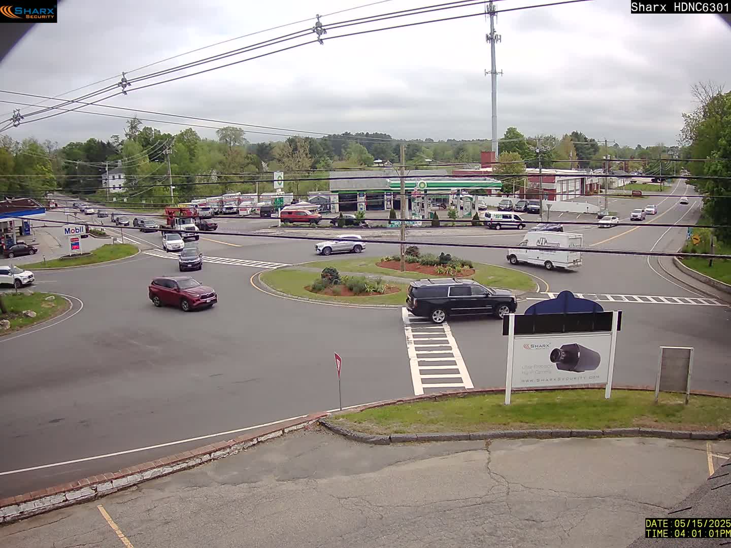 A mostly sunny day shows several vehicles navigating a roundabout and surrounding roadways near gas stations and commercial buildings.