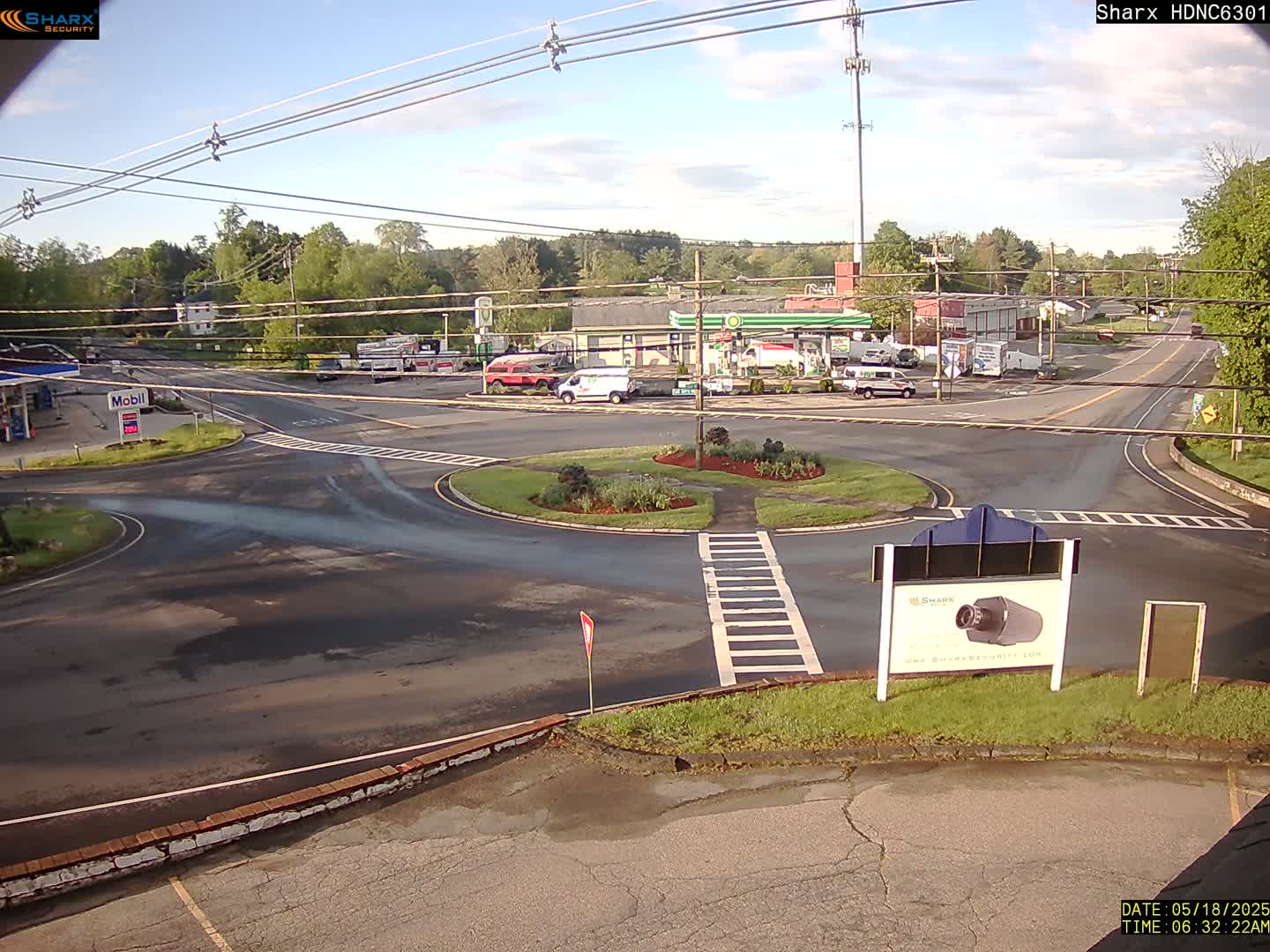A gas station and surrounding roads are visible, with a few cars present under a mostly sunny sky.
