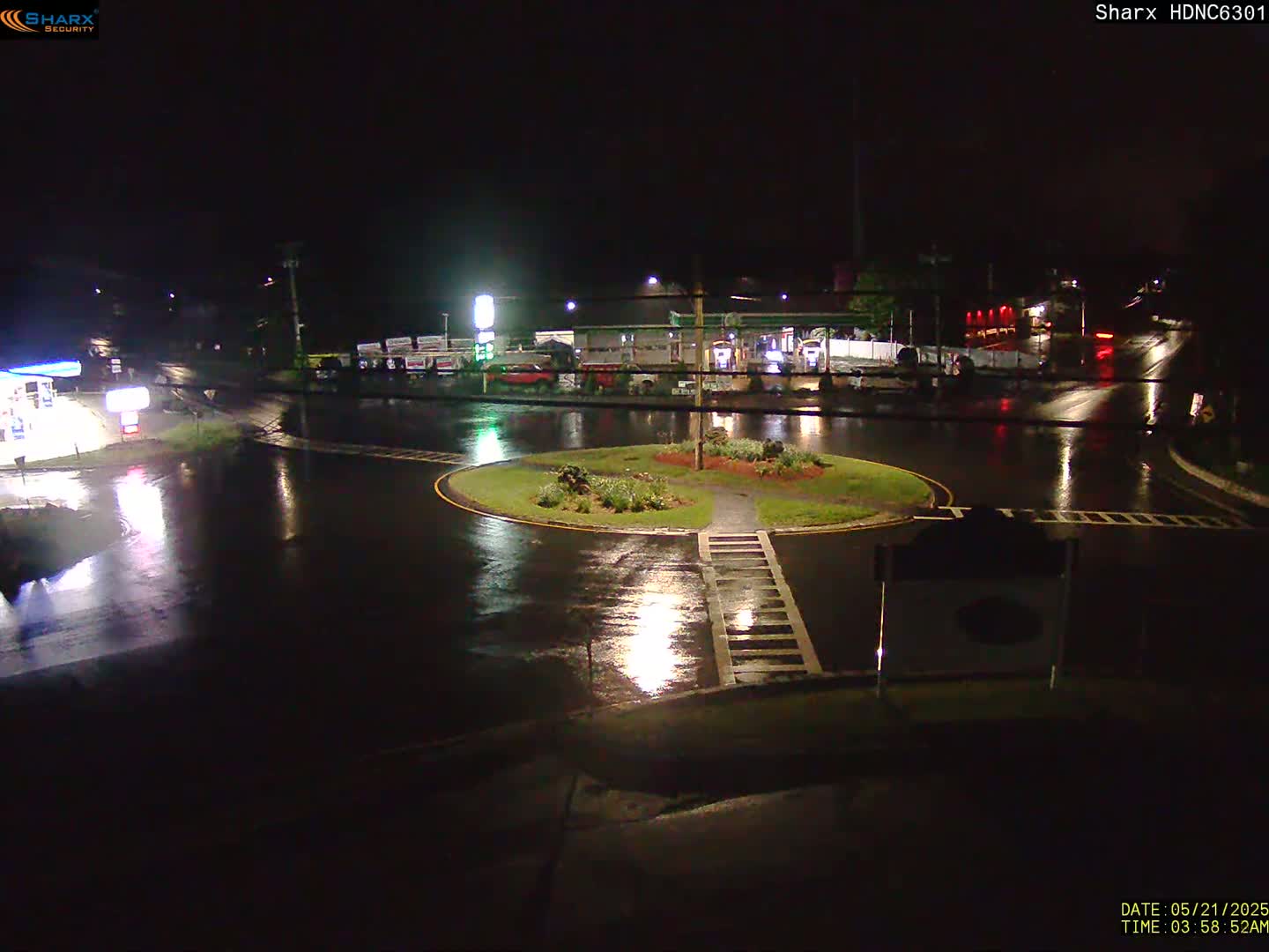 A rain-slicked roundabout at night, surrounded by businesses and illuminated by streetlights.