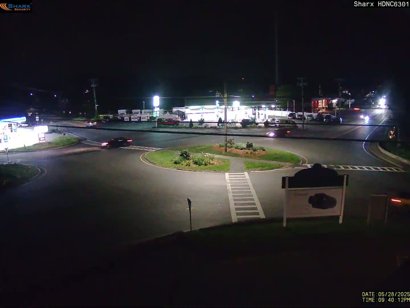A nighttime view of a gas station and roundabout with several cars present under dark skies.