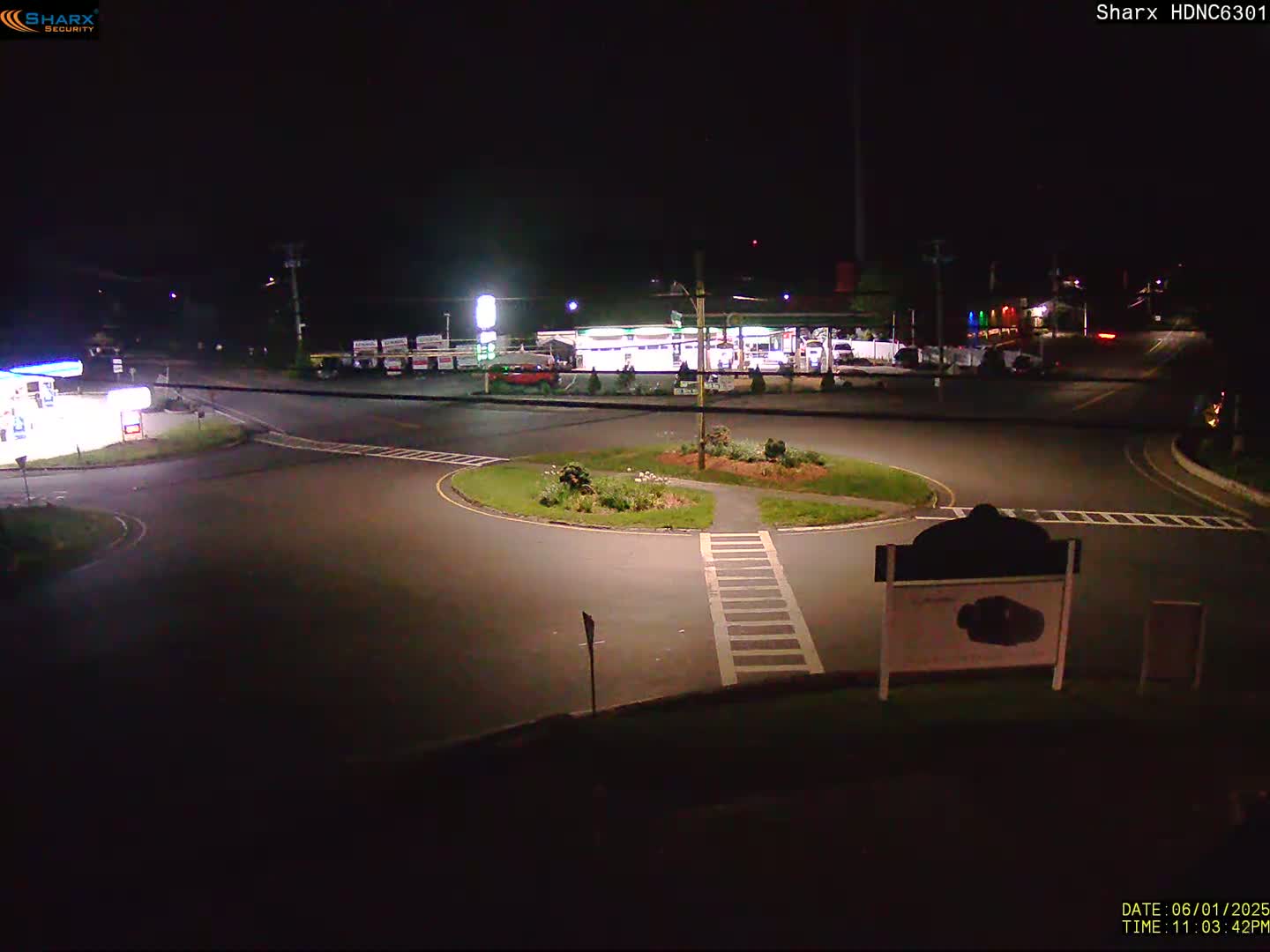 A nighttime view of a gas station and roundabout, with minimal traffic.