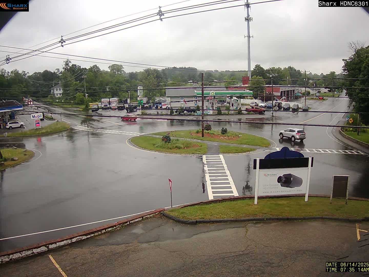 A wet, overcast day at a gas station and roundabout intersection, with several vehicles present.