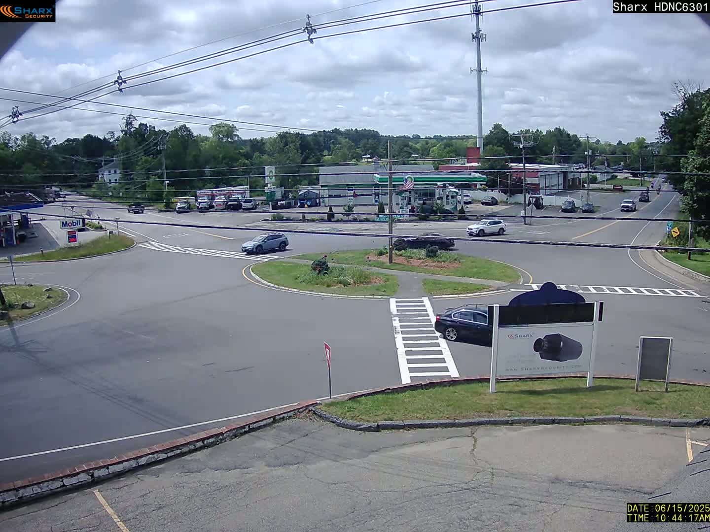 A partly cloudy day shows a view of a multi-lane roadway intersection with several vehicles and businesses, including a gas station, visible in the surrounding area.