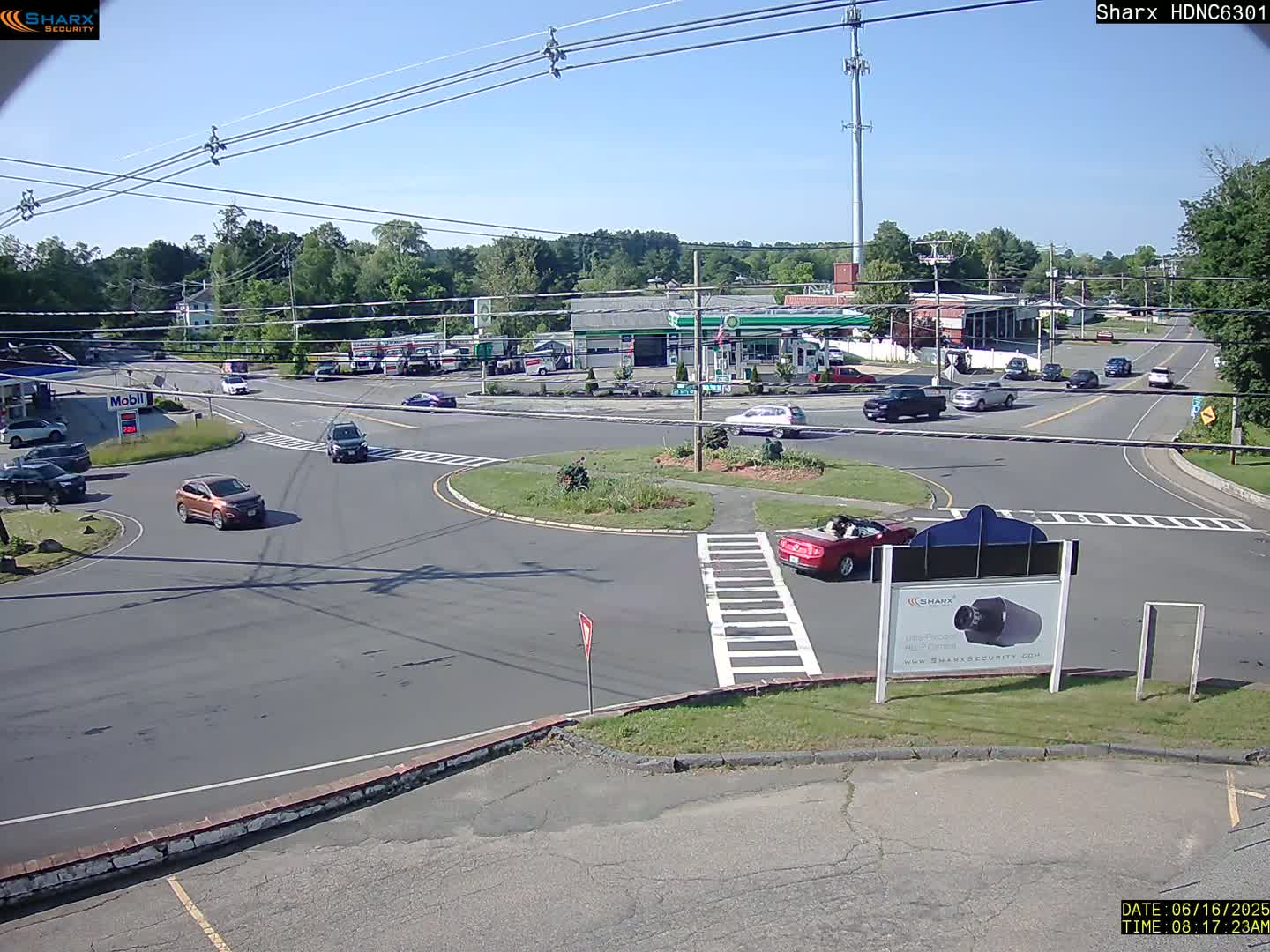 A sunny day at a gas station intersection with several cars driving around a rotary.