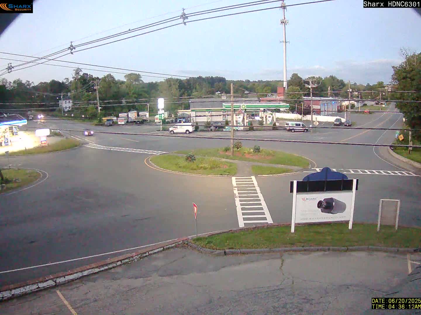 A mostly empty gas station and roundabout are visible in the early morning, under a partly cloudy sky.
