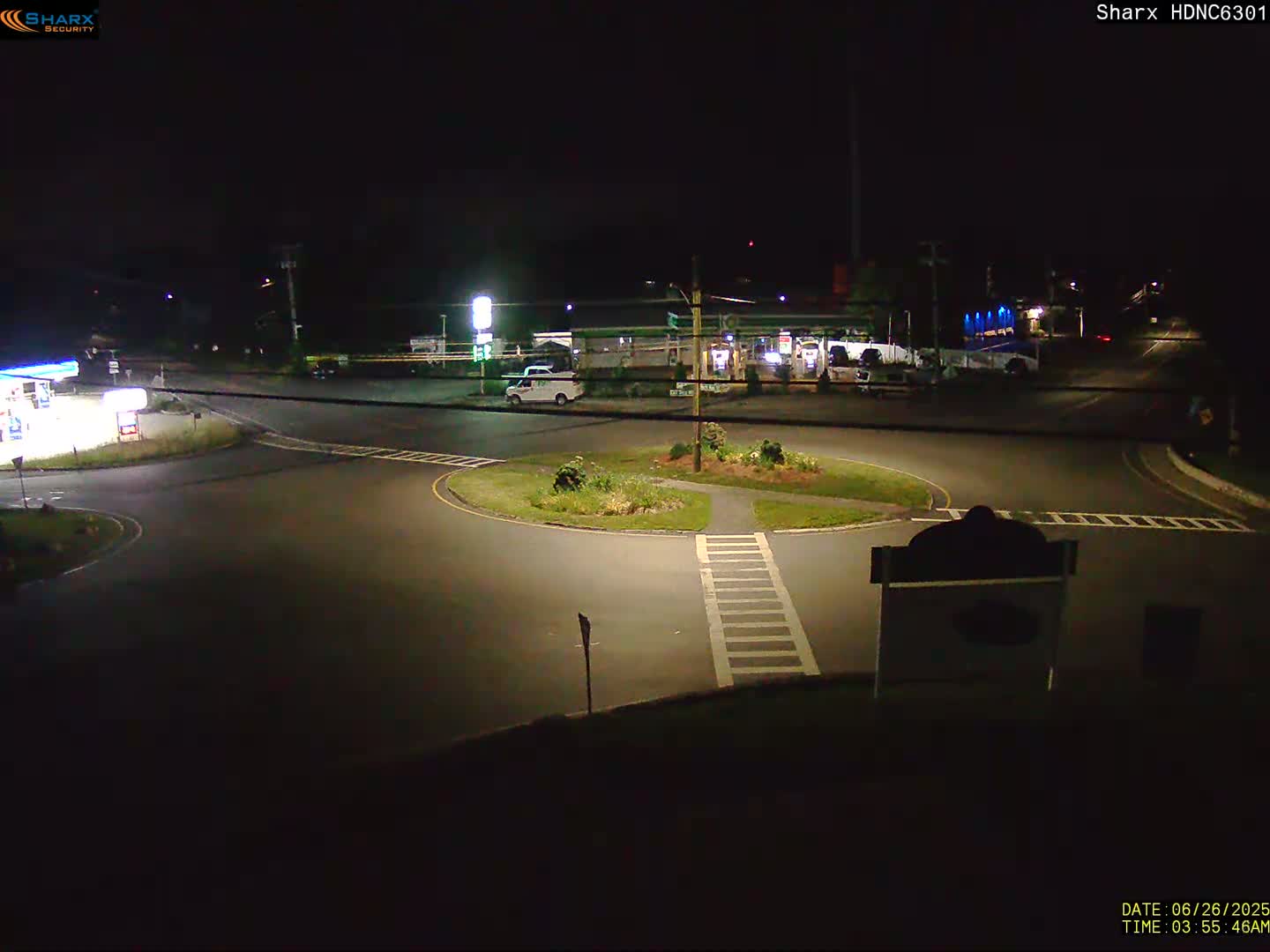 A nighttime view of a gas station and roundabout with minimal traffic under clear skies.