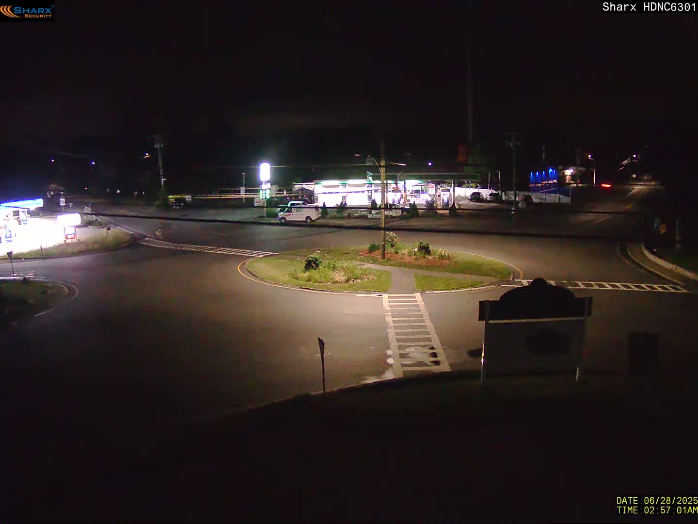 A nighttime view of a gas station and roundabout with minimal traffic.