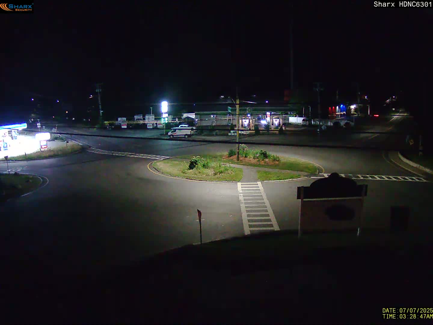 A nighttime view of a dark, mostly empty roundabout next to a gas station under artificial light.