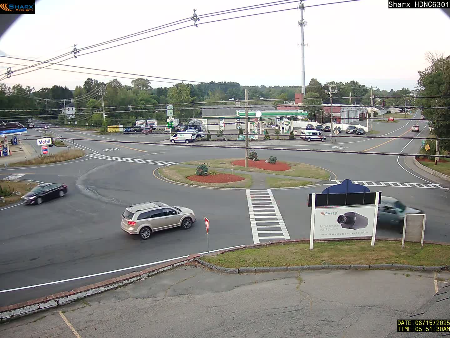 A nighttime view of a roundabout near a gas station and other businesses, with one car visible in the roundabout.