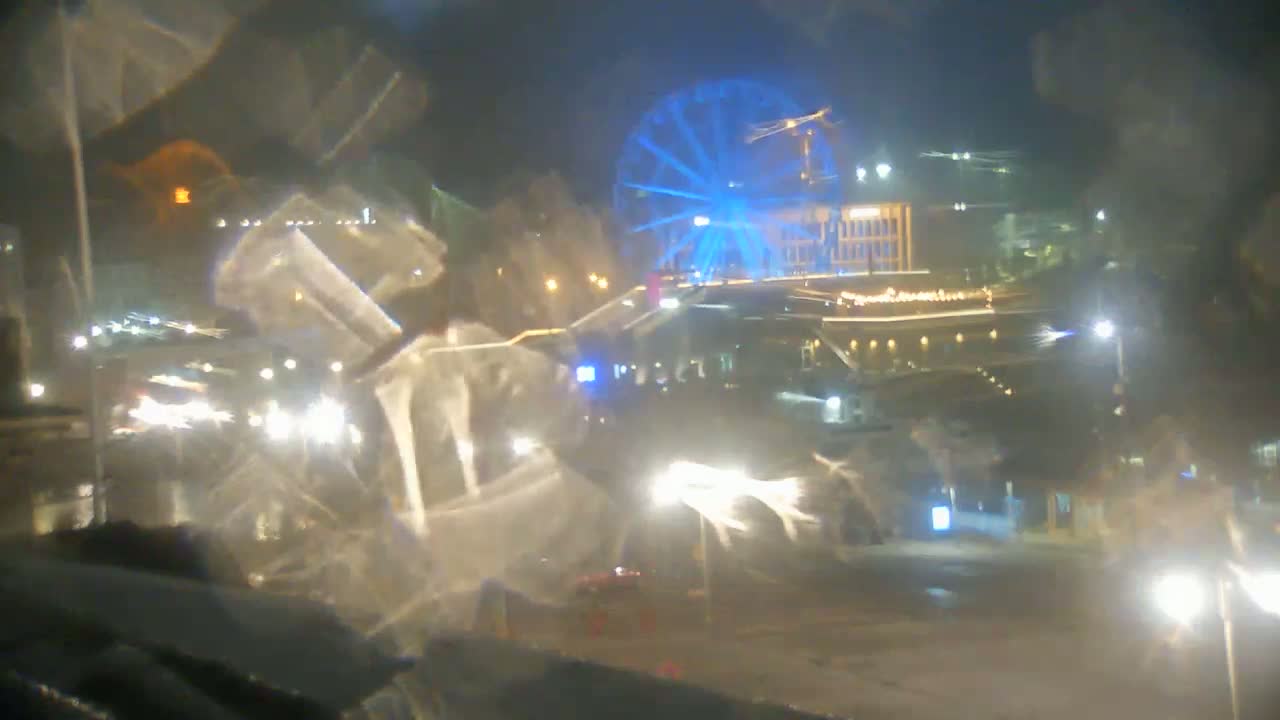 A nighttime view of a city street scene, blurred by rain or condensation on a window, shows a Ferris wheel illuminated in blue.