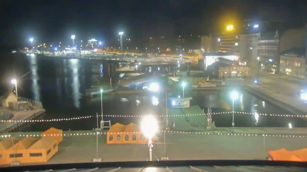 A nighttime view of a harbor with boats, buildings, and orange tents illuminated by artificial lights.