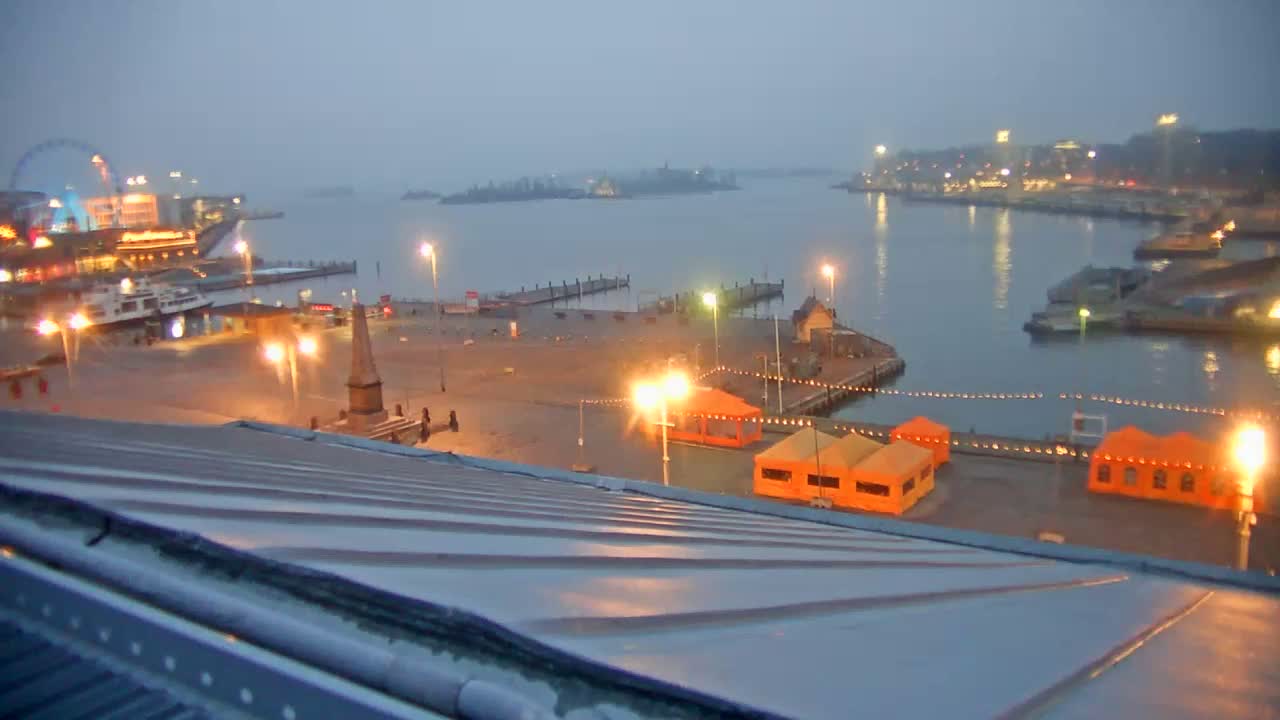 A nighttime view from a rooftop shows a harbor with illuminated docks, boats, and buildings under a hazy sky.