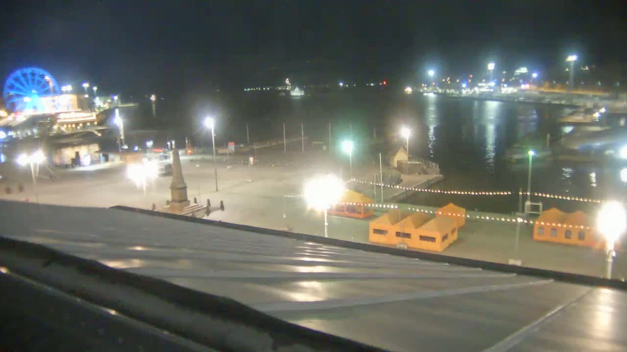 A nighttime view of a waterfront area with a Ferris wheel, illuminated structures, and calm water.