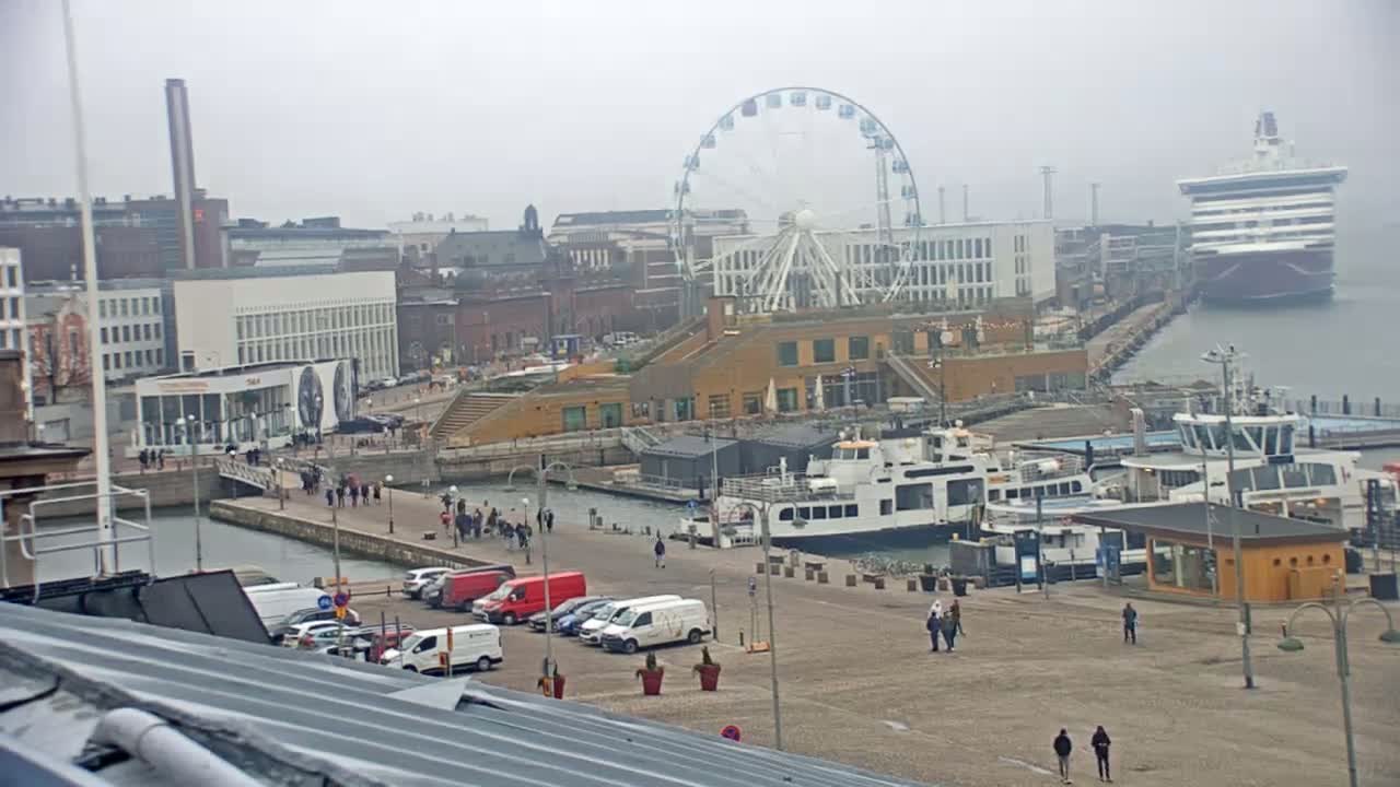 A harbor scene on an overcast day shows a Ferris wheel, several docked boats, buildings, and a cruise ship in the distance.