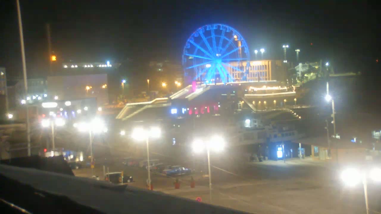 A brightly lit Ferris wheel stands at night among a collection of buildings and streetlights.