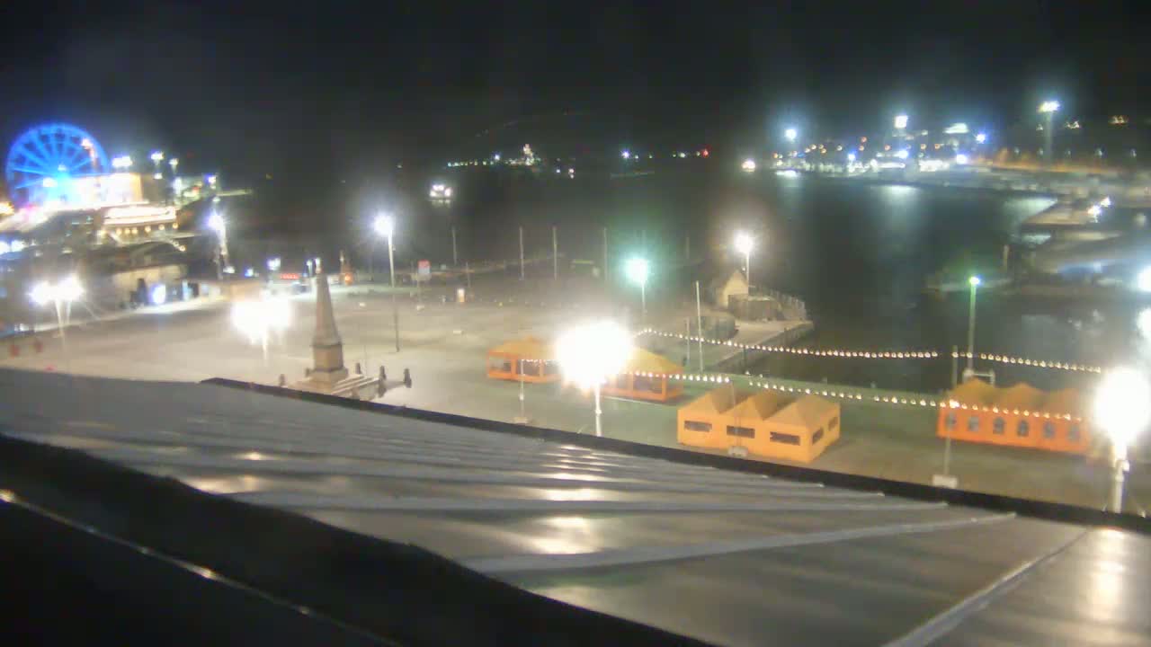 A nighttime view of a waterfront area with a Ferris wheel, illuminated structures, and calm water.