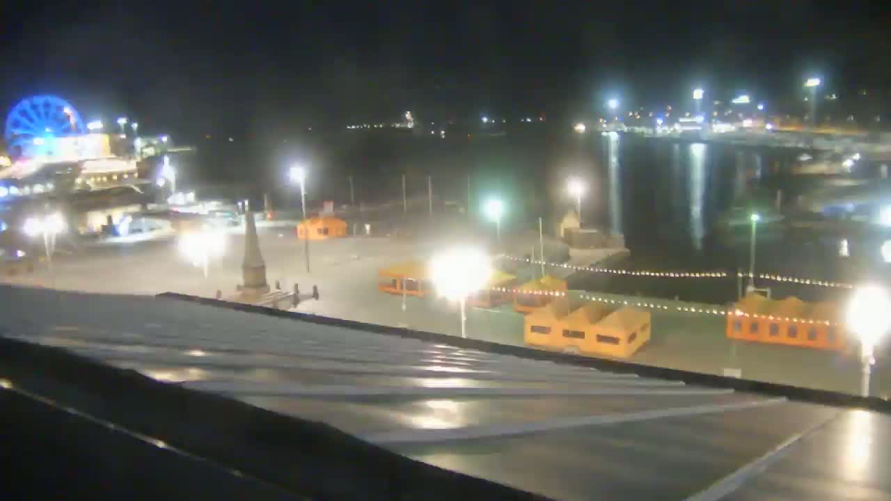 A nighttime view of a waterfront area with a Ferris wheel, illuminated structures, and calm water.