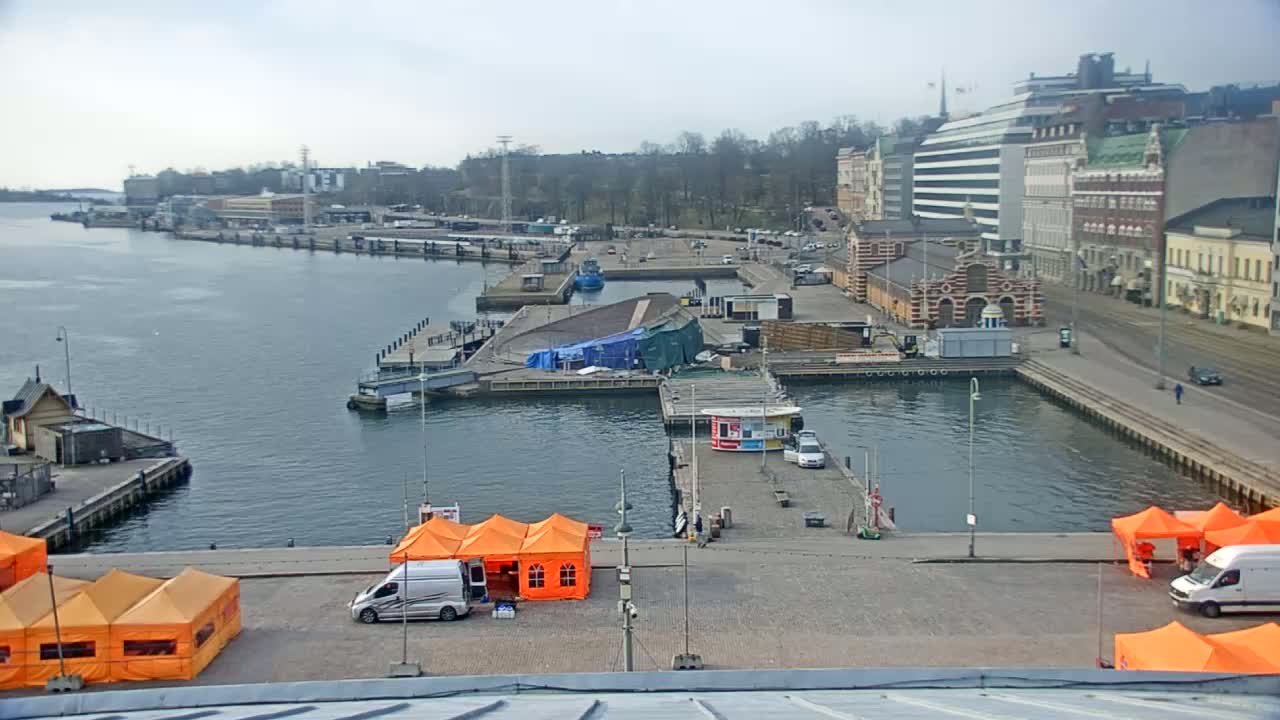 A harbor scene on a cloudy day shows a body of water with docks, buildings, and several orange tents.