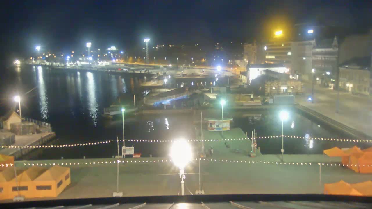 A nighttime view of a harbor with boats, buildings, and small tents illuminated by artificial lights.