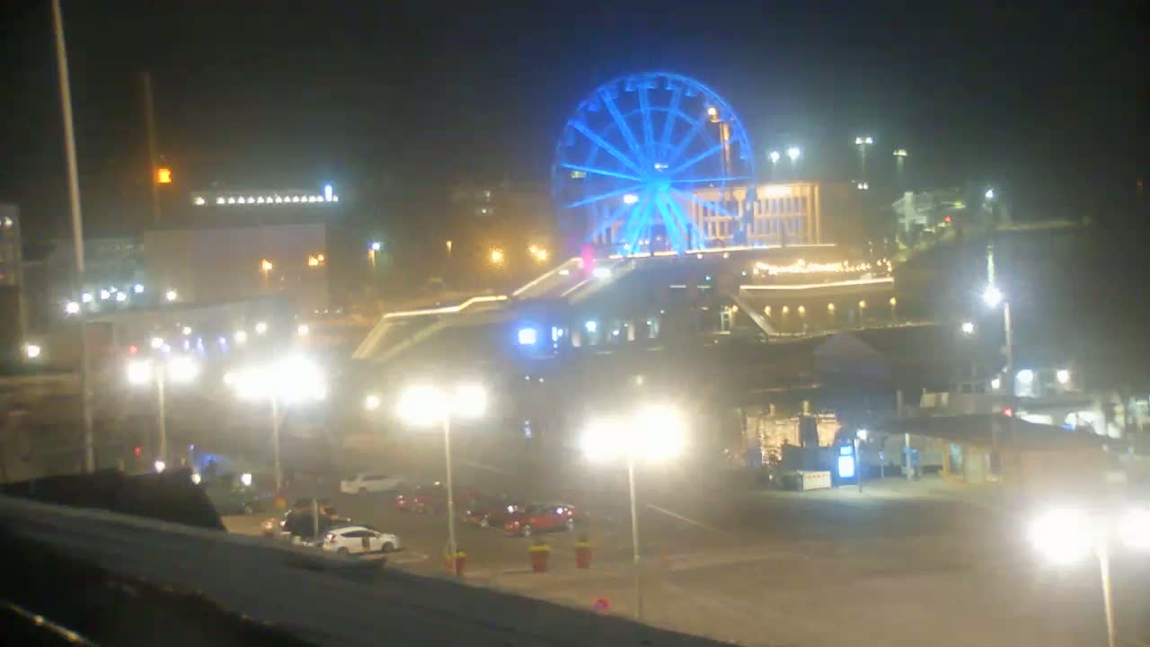 A brightly lit Ferris wheel with blue lights is visible at night, along with a parking lot, buildings, and streetlights.