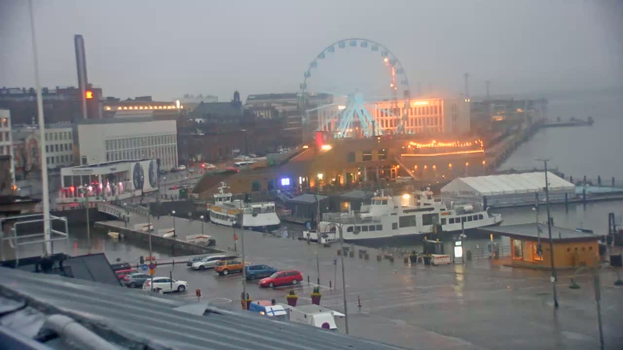 A rainy view of a harbor with ferries, a Ferris wheel, and buildings, all under a gray sky.