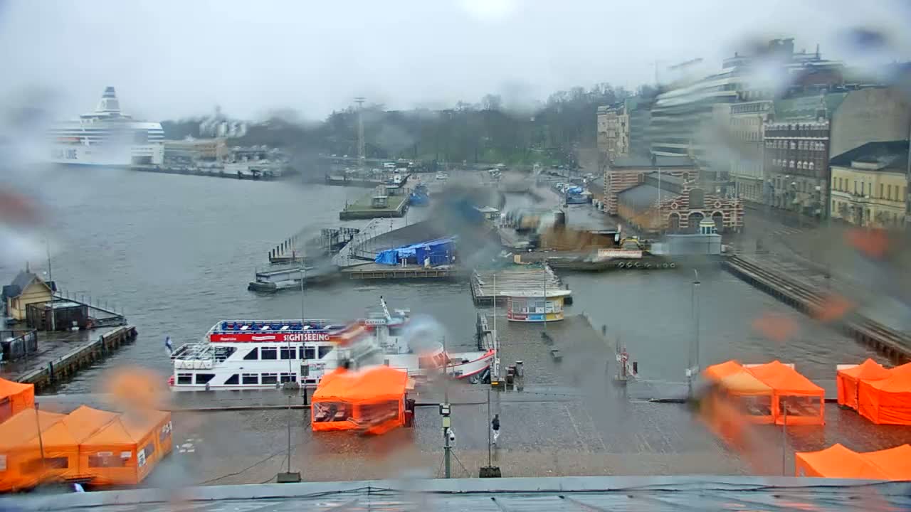 A rain-soaked harbor scene shows several boats moored near a waterfront city under a gray sky.