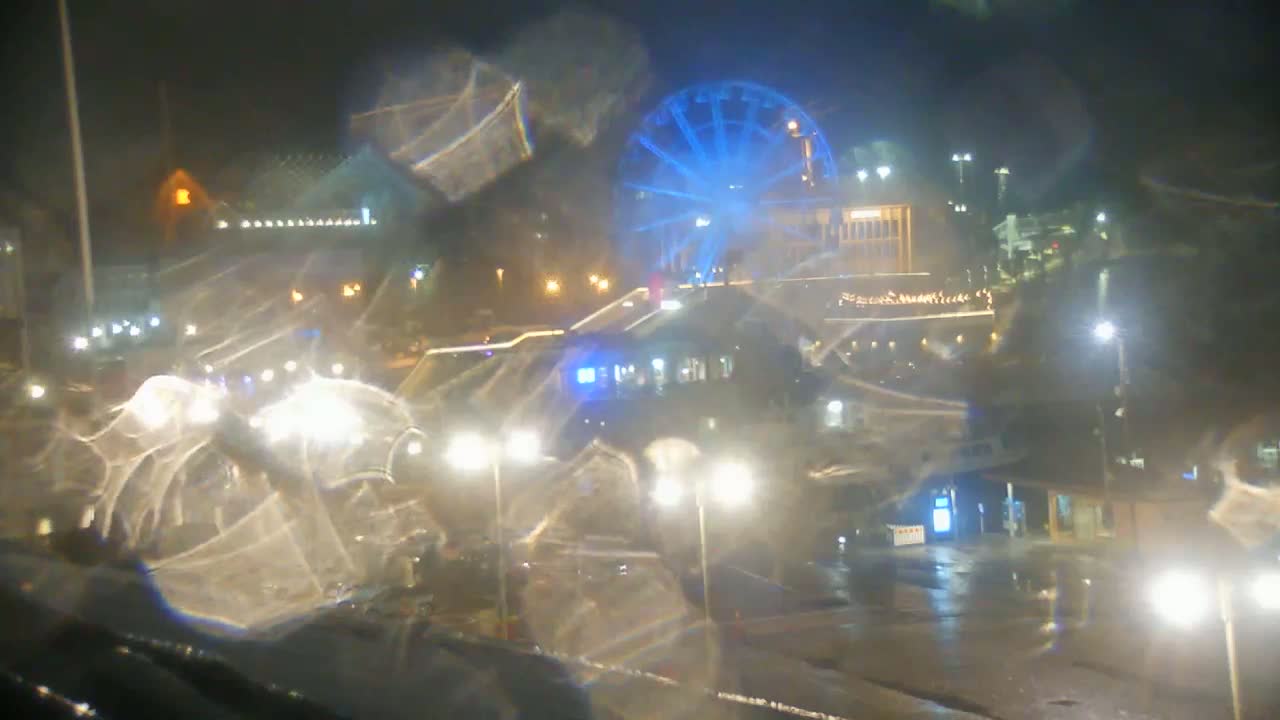 A rain-streaked nighttime view of a brightly lit Ferris wheel and city streets.