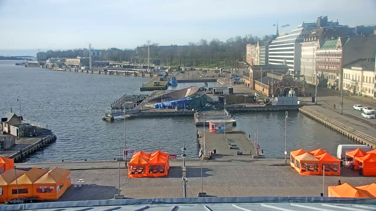 A harbor scene on a sunny day shows calm water, several piers with orange tents, and buildings along the waterfront.