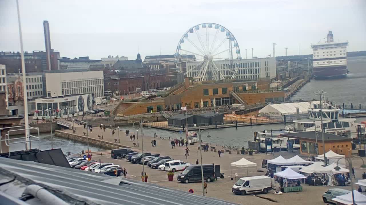 A harbor scene on an overcast day shows a Ferris wheel, buildings, a cruise ship, several boats, and a market with white tents.
