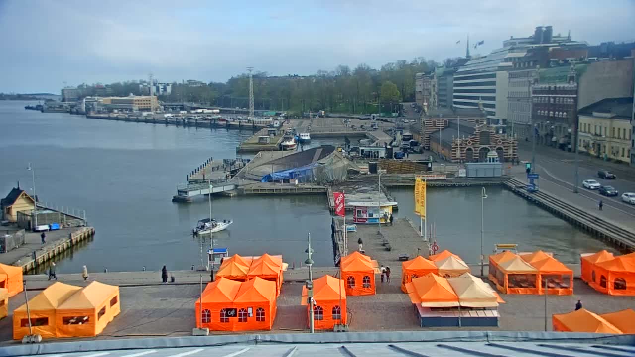 An overcast day reveals a harbor scene with numerous orange tents set up on a dock, boats moored in the water, and buildings lining the waterfront.
