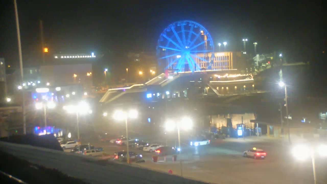 A brightly lit Ferris wheel glows blue at night in a parking lot with several cars and streetlights.