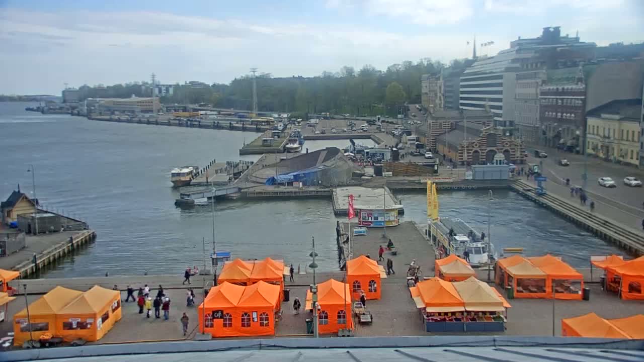 An overcast day shows a harbor with boats, buildings, and numerous orange tents set up on a dock.