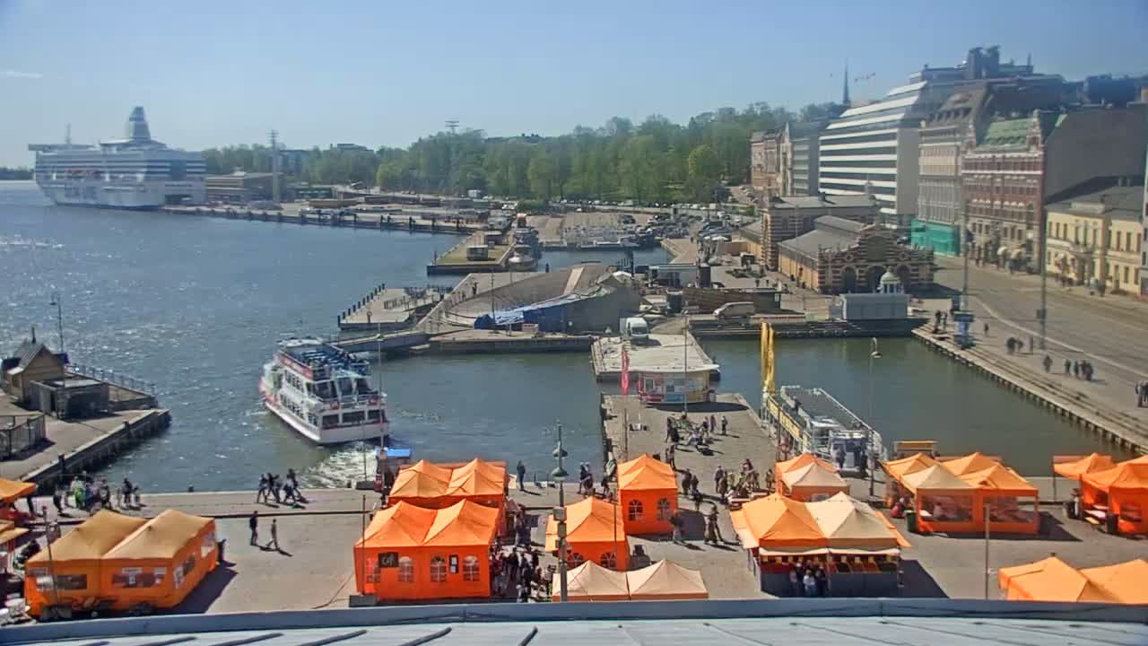 A harbor scene on a sunny day shows several boats, a large cruise ship, buildings, and numerous orange market tents.