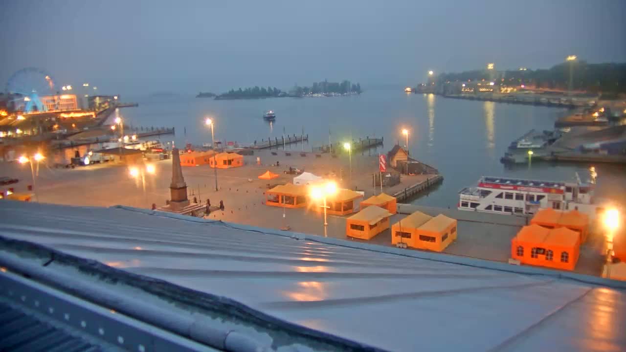 A harbor at twilight, with numerous orange tents and a large boat, under a hazy sky.