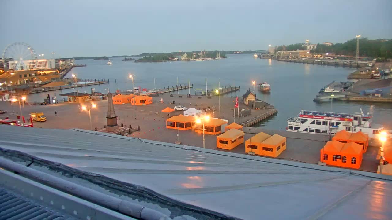An evening harbor scene with numerous orange tents in a square, boats docked, and a Ferris wheel visible in the distance under a dusky sky.