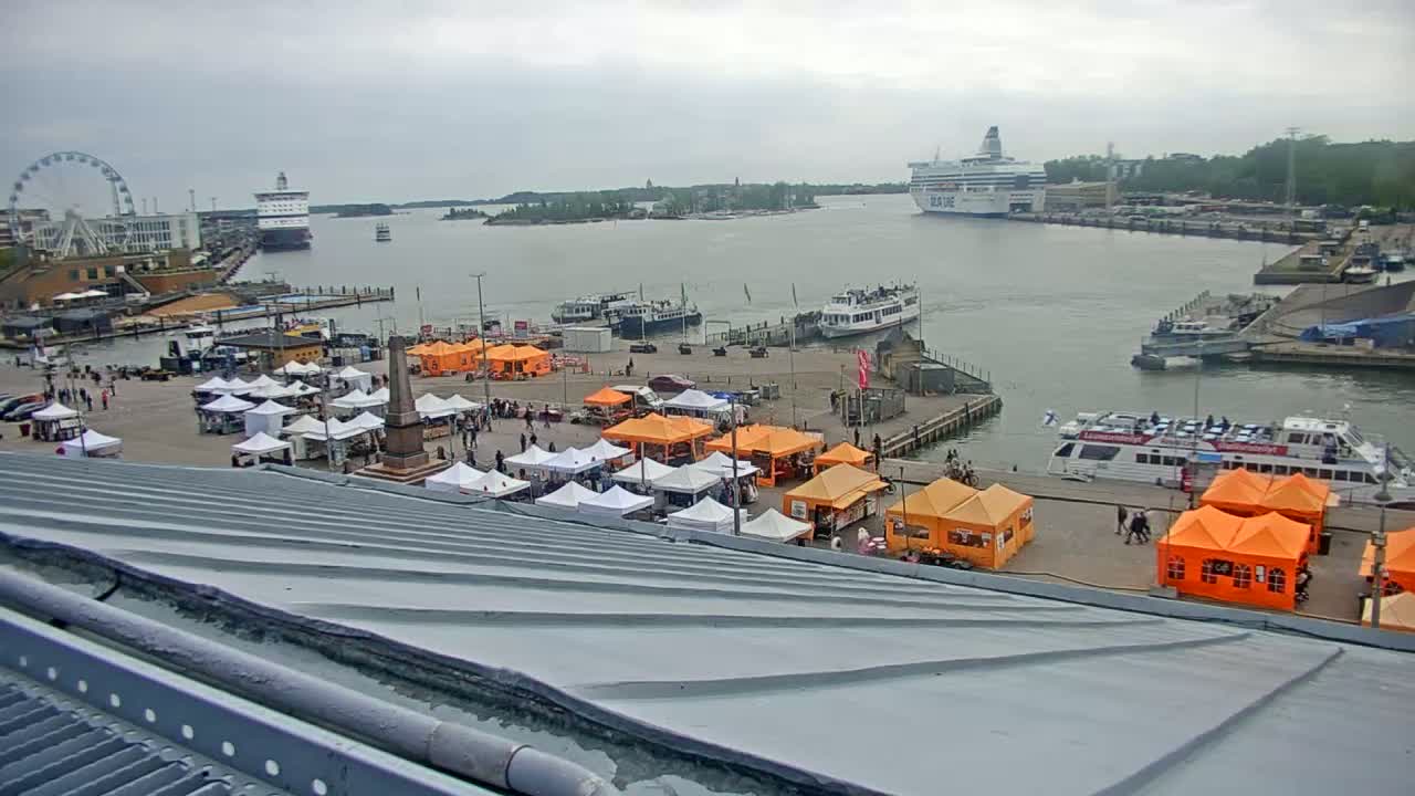 An overcast day reveals a harbor scene with numerous boats, a Ferris wheel, and a market filled with orange and white tents.