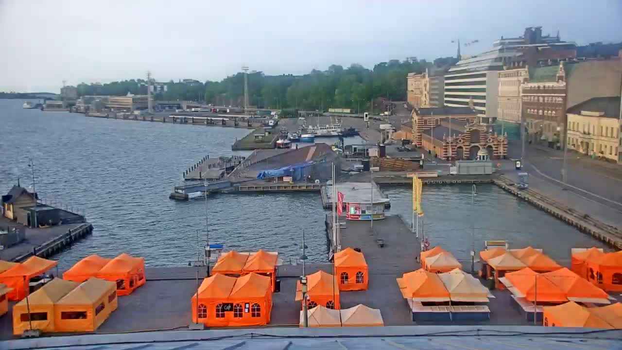 An overcast day reveals a harbor scene with numerous orange tents lining a pier, boats moored in the water, and buildings along the waterfront.