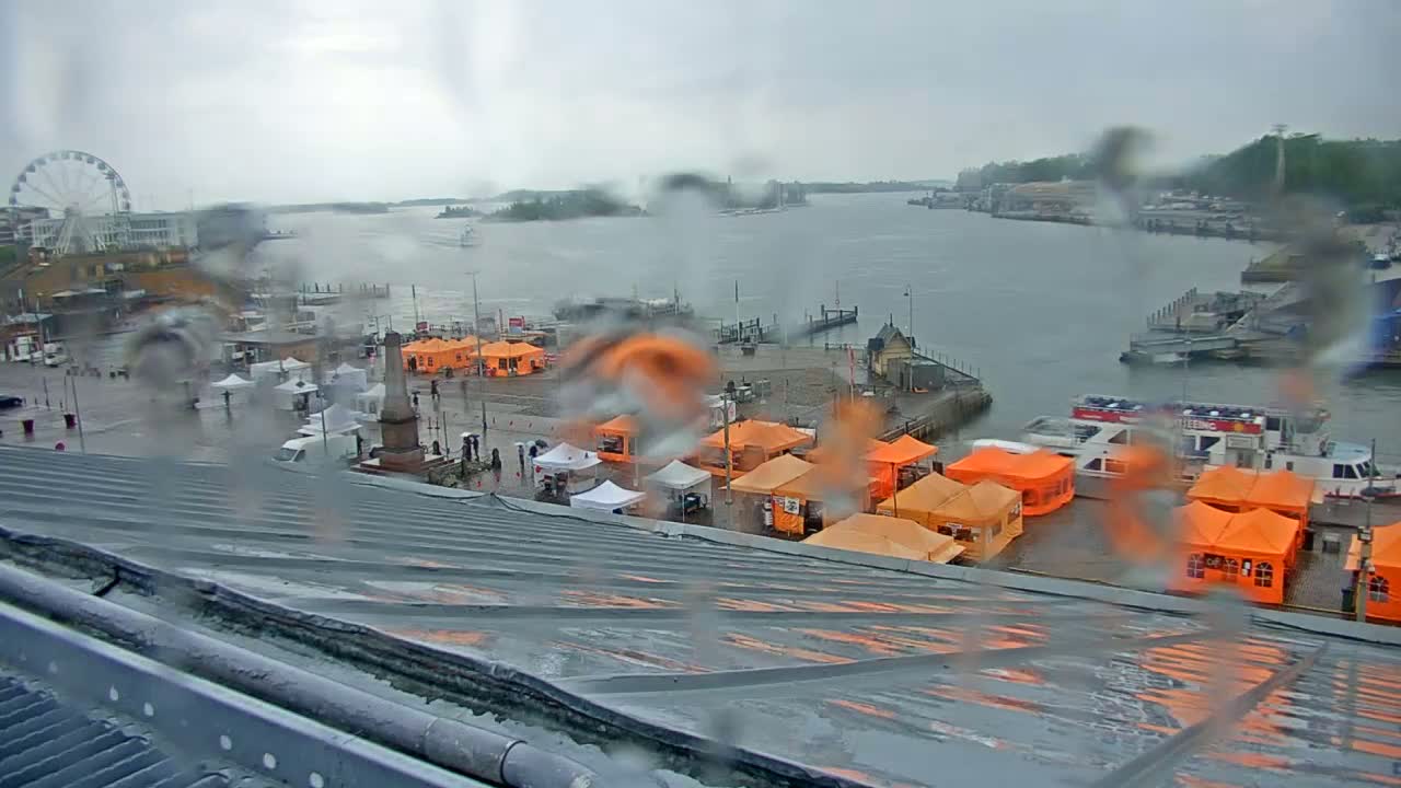 A rainy view from a rooftop shows a waterfront area with numerous orange tents, a Ferris wheel, and boats on the water.