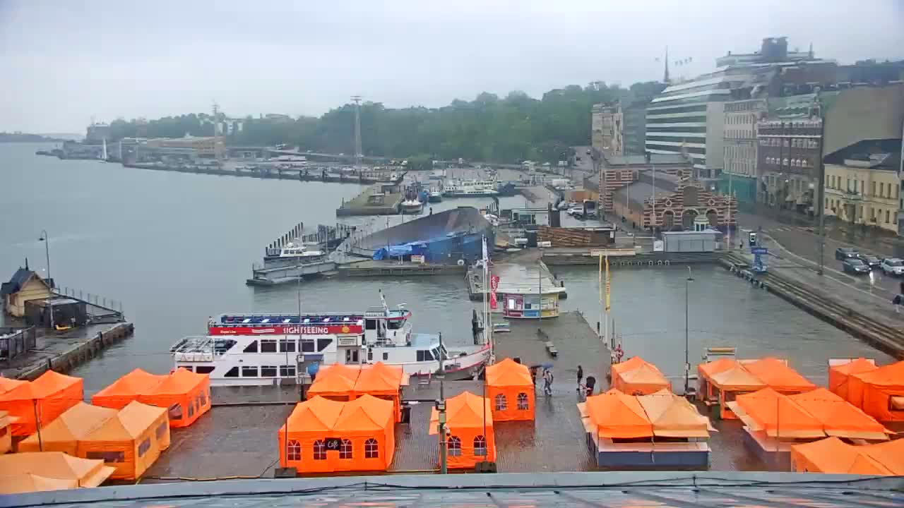 A harbor scene on a rainy day shows several boats docked near orange tents, buildings, and a roadway.