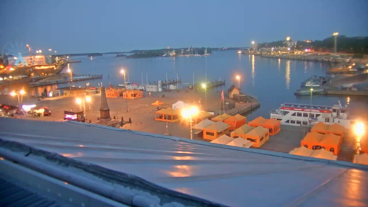 A harbor at twilight, with numerous orange tents and a large passenger boat docked, under a clear, dark sky.