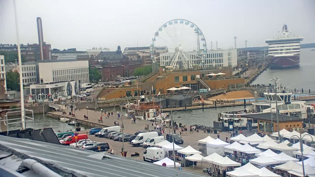 A harbor scene on an overcast day shows a Ferris wheel, a cruise ship, numerous market stalls, parked cars, and people walking along the waterfront.