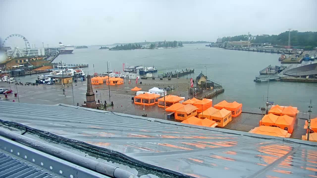 A rain-soaked harbor scene shows numerous orange tents partially submerged in water, alongside docked boats and a Ferris wheel in the distance.