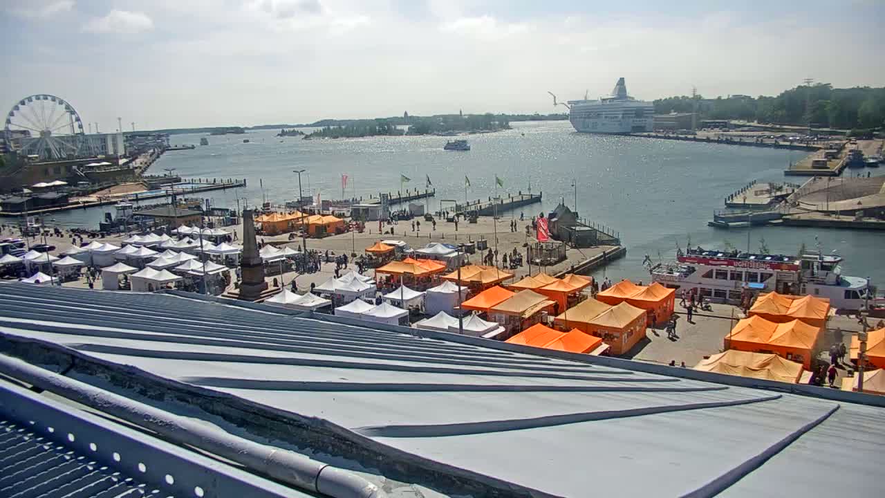A waterfront market with numerous orange and white tents is visible from a high vantage point, showcasing a harbor with a ferry and a Ferris wheel under a partly sunny sky.