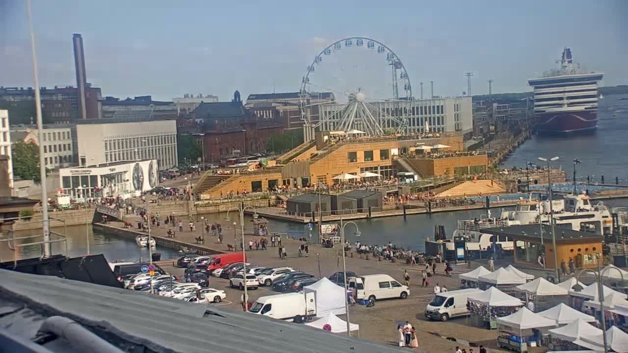 A waterfront cityscape on a sunny day features a Ferris wheel, a large cruise ship, numerous people, parked cars, market stalls, and a docked ferry.