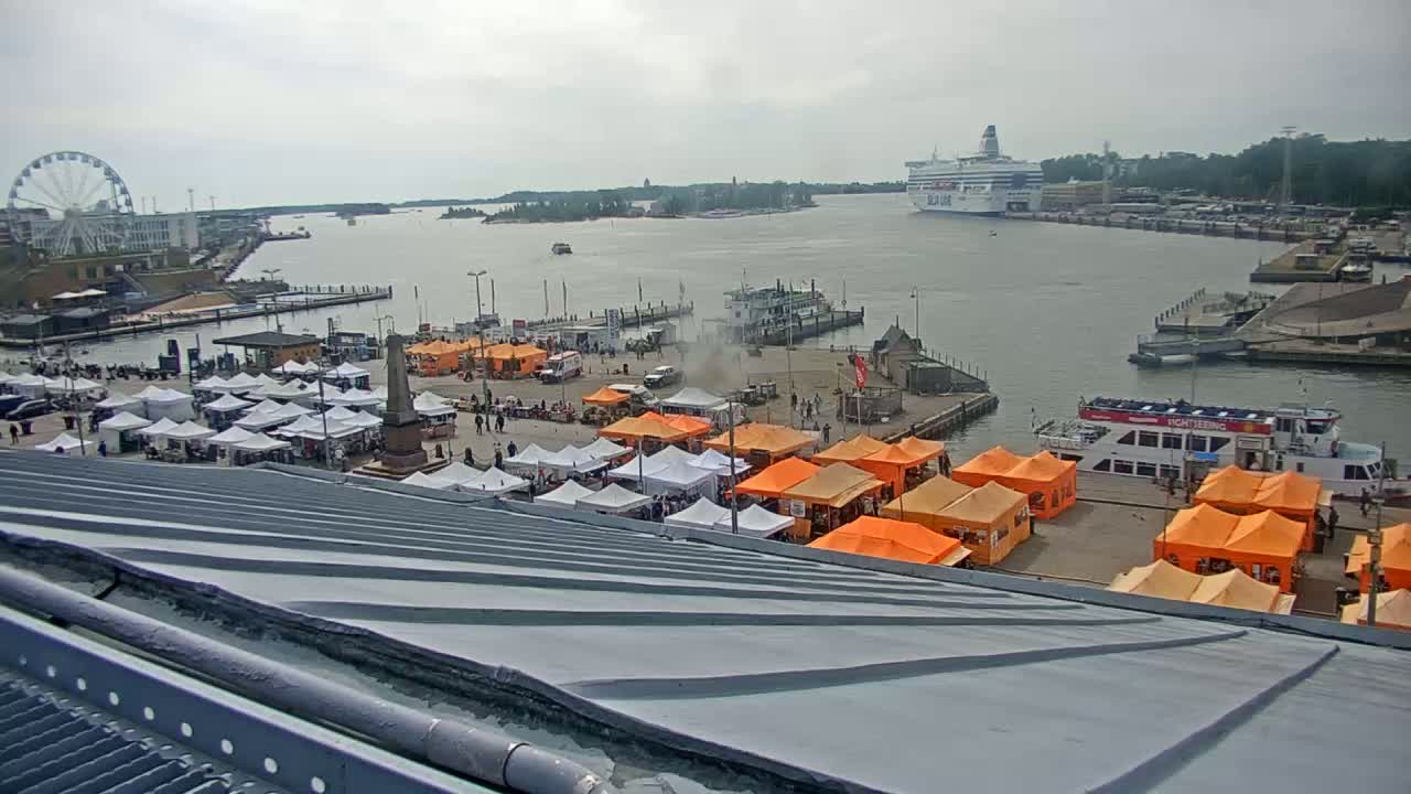 A harbor scene on an overcast day shows numerous orange and white market tents, a Ferris wheel, docked ships, and a large cruise ship in the distance.