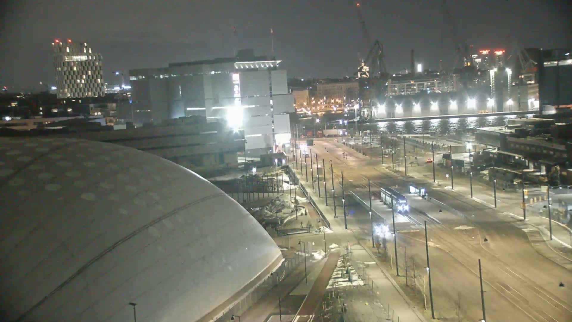 A nighttime aerial view shows a light-grey domed building next to a city street with a streetcar, and several other buildings in the background under a dark sky.