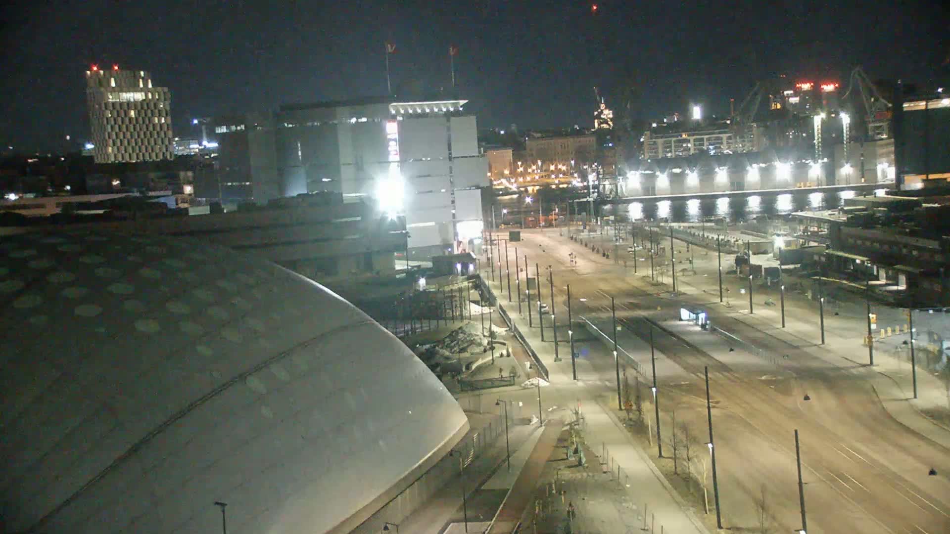 A nighttime view of a city street scene, featuring a large domed building, other buildings, and a mostly empty roadway with streetlights.
